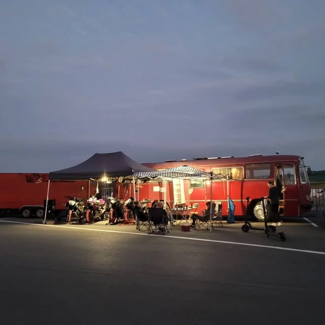 Beleuchteter roter Team-Bus und Motorräder im Fahrerlager am Abend