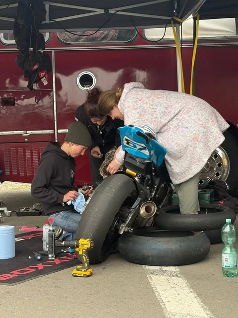 Teammitglieder bei Arbeiten an einem türkisblauen Rennmotorrad vor dem roten Bus